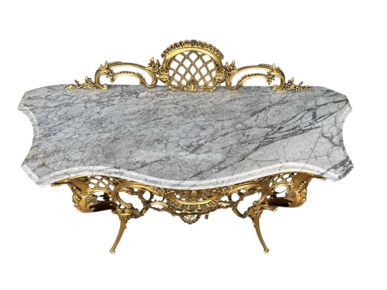 May include: An ornate, antique table with a gray marble top and gold-colored, filigree metalwork base. The table has a unique, curved shape and decorative detailing, showcasing a classic, elegant design.