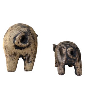 Pu&ograve; includere: Due sculture di maiale in ceramica. Il maiale pi&ugrave; grande &egrave; beige con accenti neri e una superficie strutturata. Il maiale pi&ugrave; piccolo &egrave; anch'esso beige con accenti neri e una superficie strutturata. Entrambi i maiali sono visti da dietro.