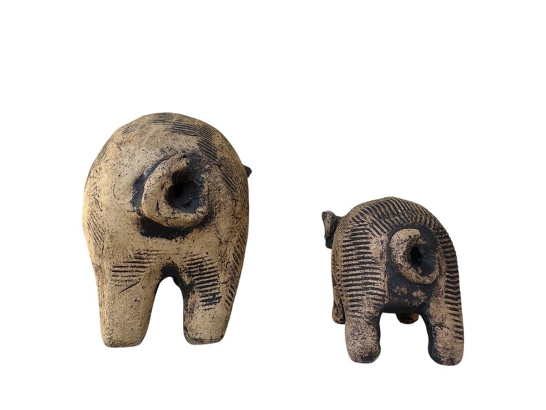 Pu&ograve; includere: Due sculture di maiale in ceramica. Il maiale pi&ugrave; grande &egrave; beige con accenti neri e una superficie strutturata. Il maiale pi&ugrave; piccolo &egrave; anch'esso beige con accenti neri e una superficie strutturata. Entrambi i maiali sono visti da dietro.