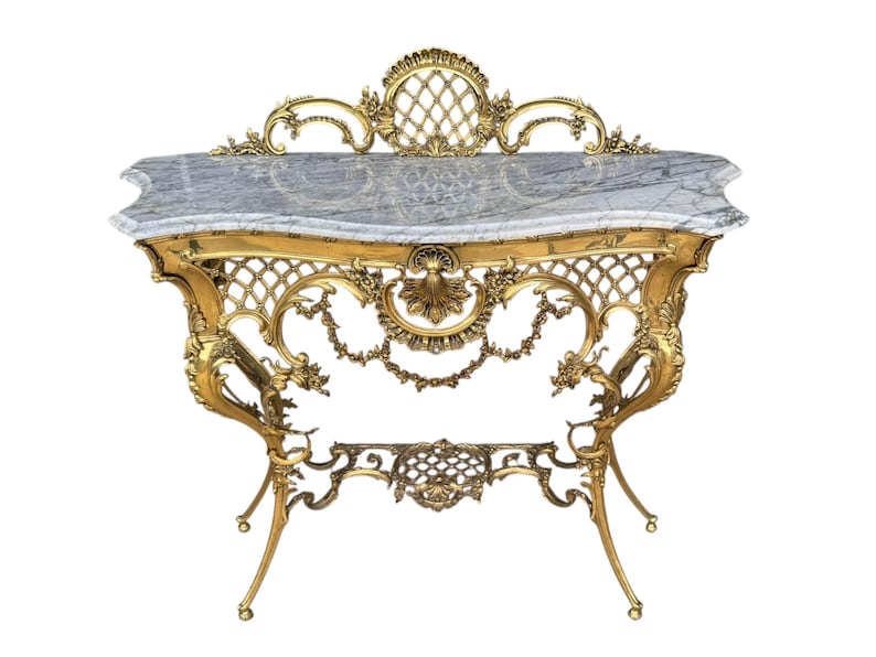 May include: Ornate gold-colored console table with a gray marble top. The table features intricate scrollwork, lattice patterns, and floral motifs. The legs are slender and curved, adding to the table's elegant design.