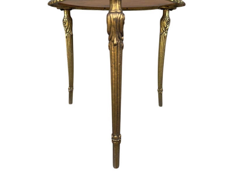 May include: A small, antique side table with a round, wooden top and three ornate, gold-coloured legs. The legs have a fluted design and decorative accents. The table is likely made of metal and wood.