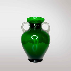 May include: A dark green glass vase with two clear glass handles. The vase has a rounded body and a narrow neck.