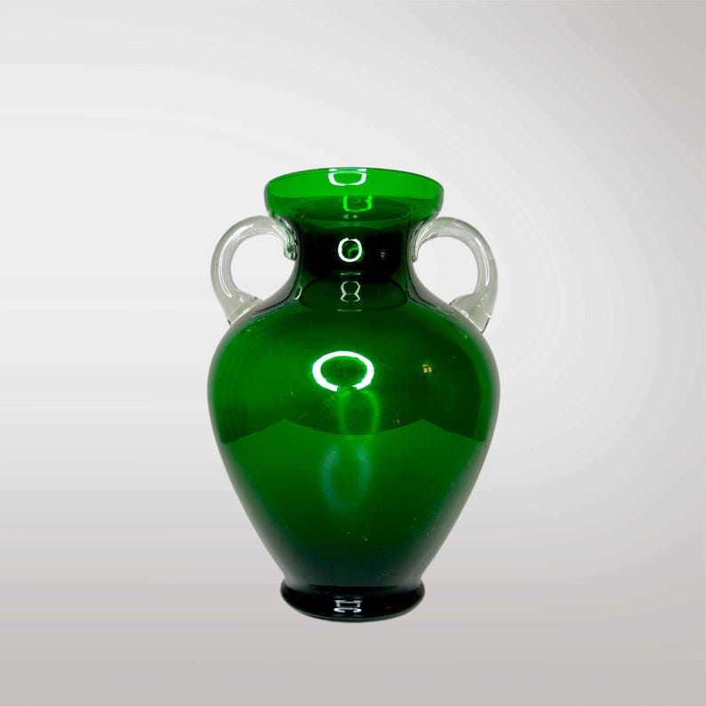 May include: A dark green glass vase with two clear glass handles. The vase has a rounded body and a narrow neck.