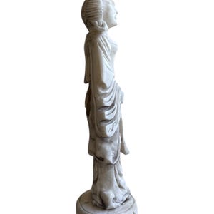 K&ouml;nnte beinhalten: Cremefarbene Statue einer Frau in flie&szlig;endem Gewand, stehend auf einem runden Sockel mit dekorativem Muster. Die Statue hat detaillierte Gesichtsz&uuml;ge und eine traditionelle Frisur. Die Figur ist im Seitenprofil, das das elegante Design zeigt.
