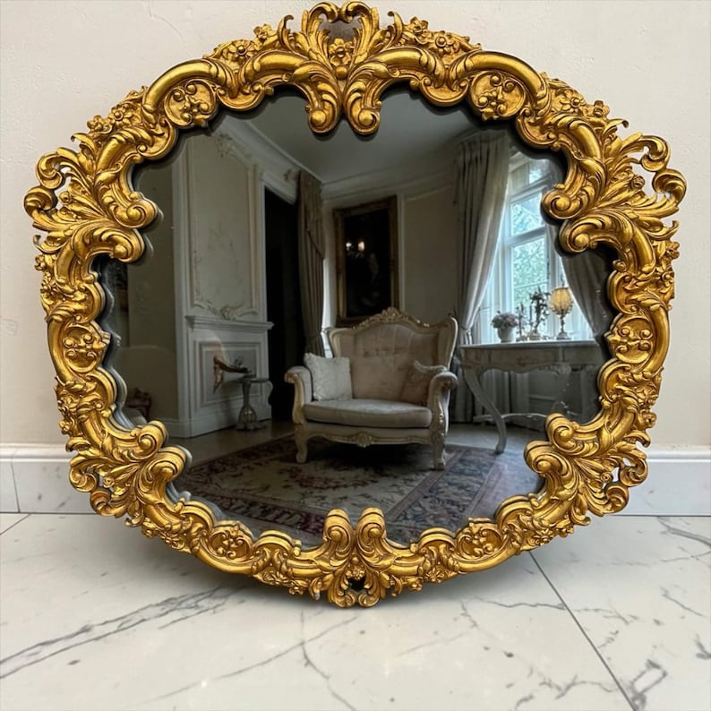 May include: Ornate, gold-colored mirror with a decorative, floral-inspired frame. The mirror has a dark reflective surface, and the frame features intricate detailing. The mirror is a decorative piece for a home.