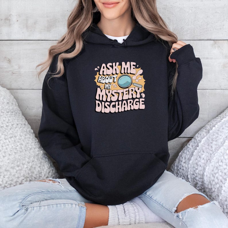 Peut inclure: Sweat-shirt &agrave; capuche noir avec un imprim&eacute; graphique d'une loupe et le texte "Ask me about my mystery discharge".