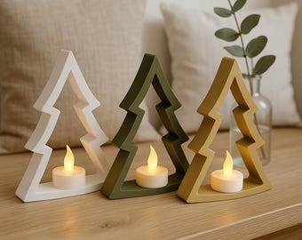 Puede incluir: Tres candelabros decorativos en forma de árbol, en blanco, verde oliva y amarillo mostaza. Cada soporte tiene una pequeña vela a pilas, creando un brillo cálido. Los candelabros están colocados sobre una superficie de madera.