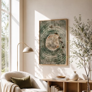 May include: A framed print of a tree trunk cross-section, displaying rings in green, brown, and beige. The artwork hangs in a room with a neutral colour scheme, alongside a comfortable armchair and wooden furnishings. The room is bathed in natural light.