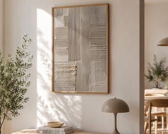 May include: A framed abstract wall art piece with a textured, light gray surface and a natural wood frame. The artwork hangs above a light wood cabinet with a lamp, books, and a decorative bowl. The room has a neutral color palette.