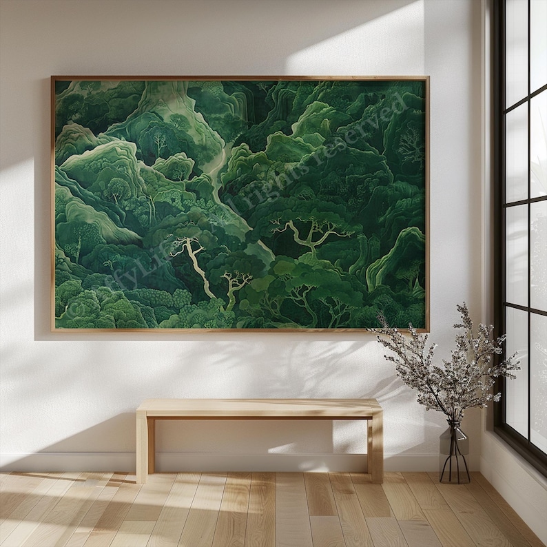 Framed painting of lush, green forest with winding paths on a white wall. Light wooden bench below; vase with twigs to the right, all in soft natural light.