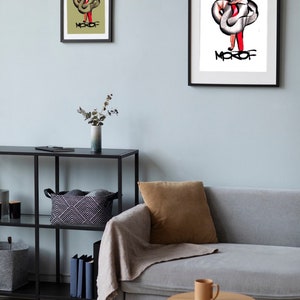 May include: Two framed illustrations of a person with a snake wrapped around them. The illustrations are in black and white with red accents. The text "MOROF" is written in black below the person in both illustrations. The illustrations are hanging on a light blue wall.