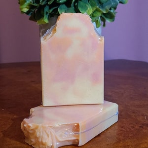 May include: Two bars of handmade soap, one with a swirl design and the other with a floral design. The soap is a light pink and white color.