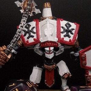 May include: A white and red painted miniature figure with a gold and black weapon and shield. The figure is standing on a black base with two red and gold dice.