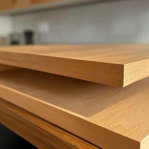 May include: Close-up of two wooden planks, likely for a table or countertop. The wood has a light brown color with visible grain, suggesting a natural finish. The edges are clean and square, indicating a modern design. The planks are stacked, showing the thickness and texture of the wood.