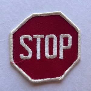 May include: A red octagonal stop sign with white stitching around the edges and the word "STOP" in white lettering.