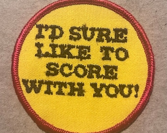May include: A yellow circle patch with a red border. The text on the patch reads "I'd sure like to score with you!"