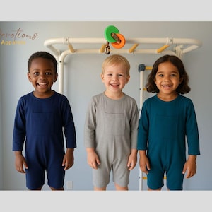 Peut inclure: Trois enfants portant des combinaisons à manches longues de différentes couleurs. L'enfant à gauche porte une combinaison bleu marine, l'enfant au milieu porte une combinaison grise et l'enfant à droite porte une combinaison turquoise. Les trois enfants sont debout devant une structure de jeu blanche.