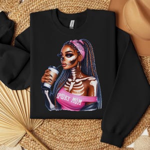 May include: Black sweatshirt with a graphic of a woman with a pink bandana and skeleton makeup. The woman is holding a coffee cup and the text "Spooky Mom" is printed on her shirt.