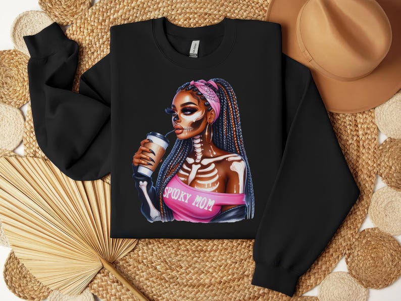 May include: Black sweatshirt with a graphic of a woman with a pink bandana and skeleton makeup. The woman is holding a coffee cup and the text "Spooky Mom" is printed on her shirt.
