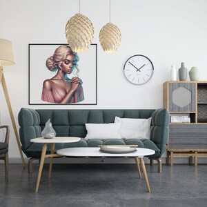 May include: A teal green sofa with a white pillow in a living room setting. A framed print of a woman with long blonde hair wearing a pink dress hangs on the wall above the sofa. There are two hanging light fixtures with a wood-like finish and a floor lamp with a beige lampshade. A wooden shelf with a geometric design and a small round table with a white top are also visible.