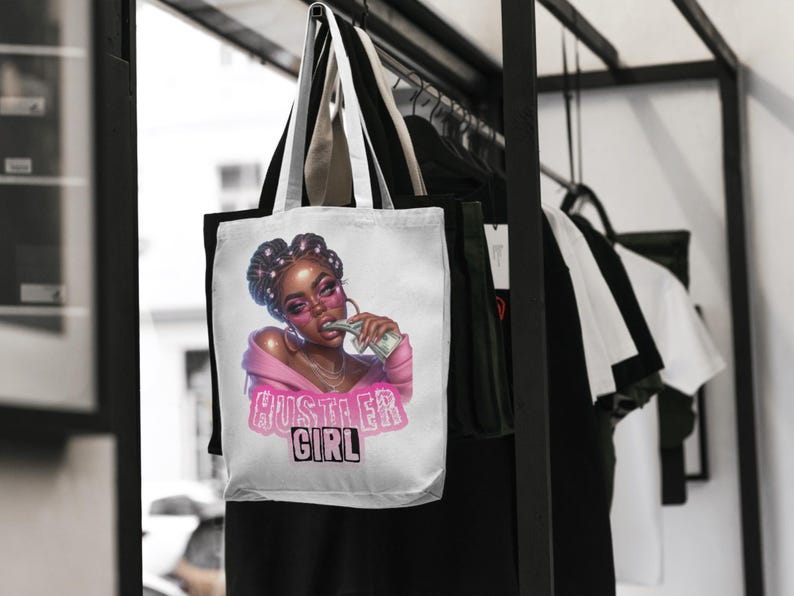 Op de afbeelding: Witte tote bag met een roze en witte illustratie van een vrouw met een zonnebril die geld in haar mond houdt. De tekst "Hustler Girl" is in roze op de tas gedrukt.