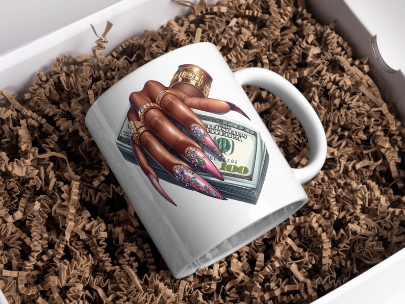 May include: White ceramic mug featuring a colourful illustration of a hand with long, glittery nails holding a stack of US dollar bills. The hand is wearing several gold rings.