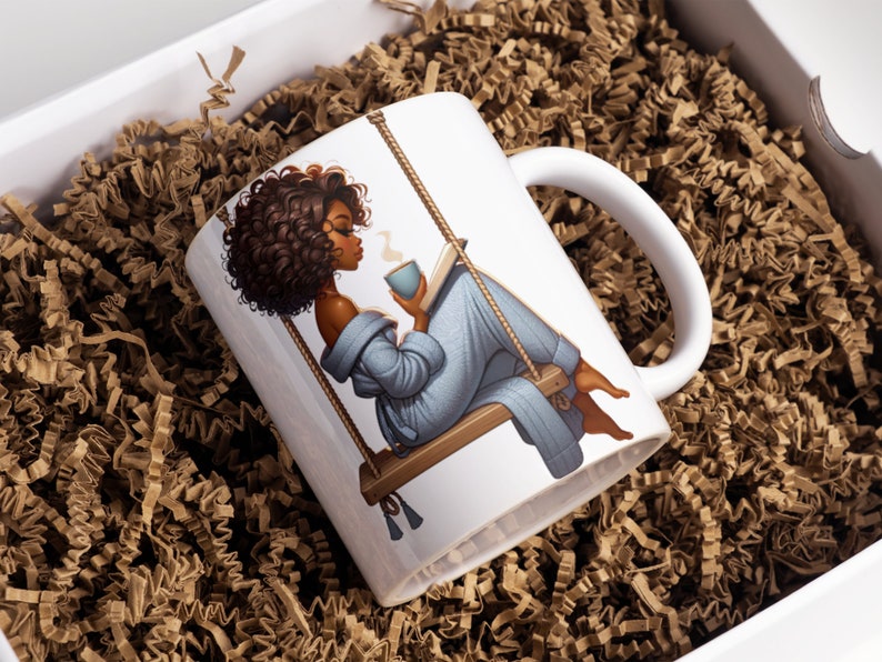 May include: White ceramic mug with a graphic of a woman with brown curly hair sitting on a swing and reading a book while holding a cup of coffee. The woman is wearing a blue robe.