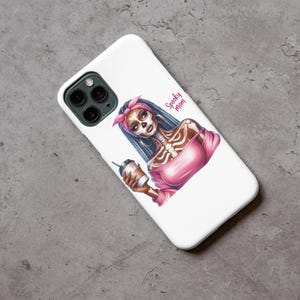 May include: White iPhone case with a colorful illustration of a skeleton woman with blue hair wearing a pink shirt and holding a coffee cup. The text "Spooky Mom" is printed on the case.