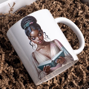 May include: White ceramic mug with a colorful illustration of a woman with dark skin reading a book. She has a floral hairpiece and is wearing a light pink and blue dress.