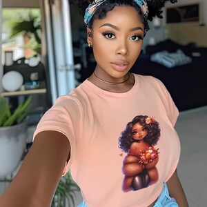 May include: A woman wearing a peach-colored t-shirt with a graphic of a cartoon woman with brown hair and a brown fur coat holding flowers. The woman in the photo is wearing a blue and white patterned headband.