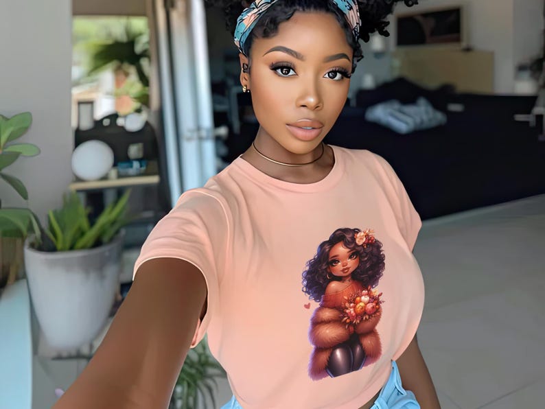 May include: A woman wearing a peach-colored t-shirt with a graphic of a cartoon woman with brown hair and a brown fur coat holding flowers. The woman in the photo is wearing a blue and white patterned headband.