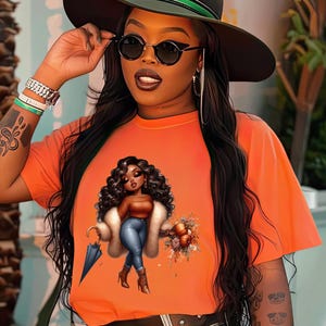 May include: A bright orange t-shirt with a graphic print of a cartoon woman holding an umbrella and a bouquet of flowers. The woman is wearing a fur coat, blue jeans, and brown boots.