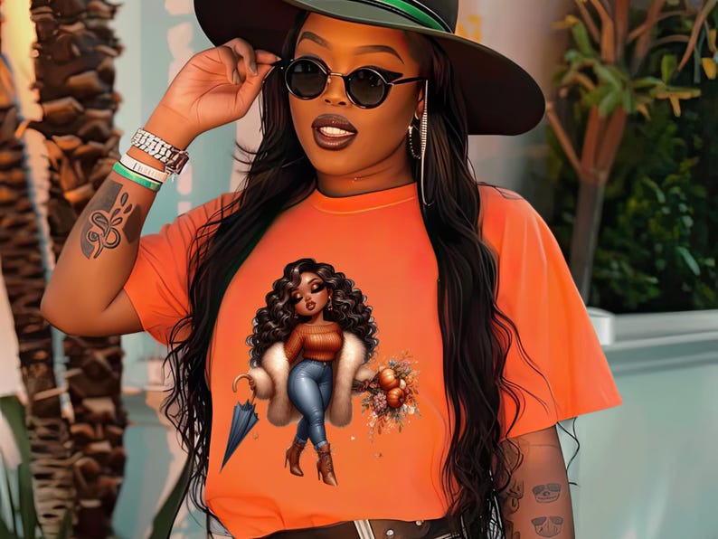 May include: A bright orange t-shirt with a graphic print of a cartoon woman holding an umbrella and a bouquet of flowers. The woman is wearing a fur coat, blue jeans, and brown boots.