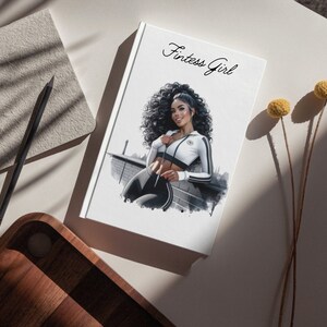 May include: A white notebook with the text "Fitnes Girl" on the cover. The notebook features a black and white illustration of a woman wearing a white and black athletic outfit.