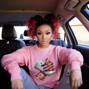 May include: A woman wearing a pink sweatshirt with a graphic of a hand holding a wad of money. The hand is adorned with gold rings and long, manicured nails.