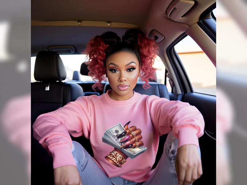 May include: A woman wearing a pink sweatshirt with a graphic of a hand holding a wad of money. The hand is adorned with gold rings and long, manicured nails.