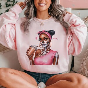 May include: Pink sweatshirt with a graphic of a woman with a skeleton face, wearing a pink shirt and holding a cup of coffee. The text "MOM." is printed on the sweatshirt.