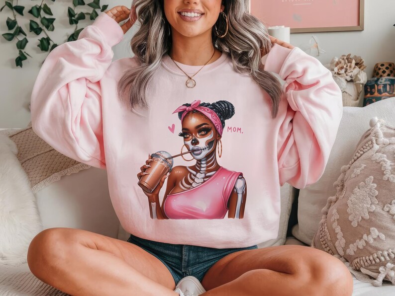 May include: Pink sweatshirt with a graphic of a woman with a skeleton face, wearing a pink shirt and holding a cup of coffee. The text "MOM." is printed on the sweatshirt.