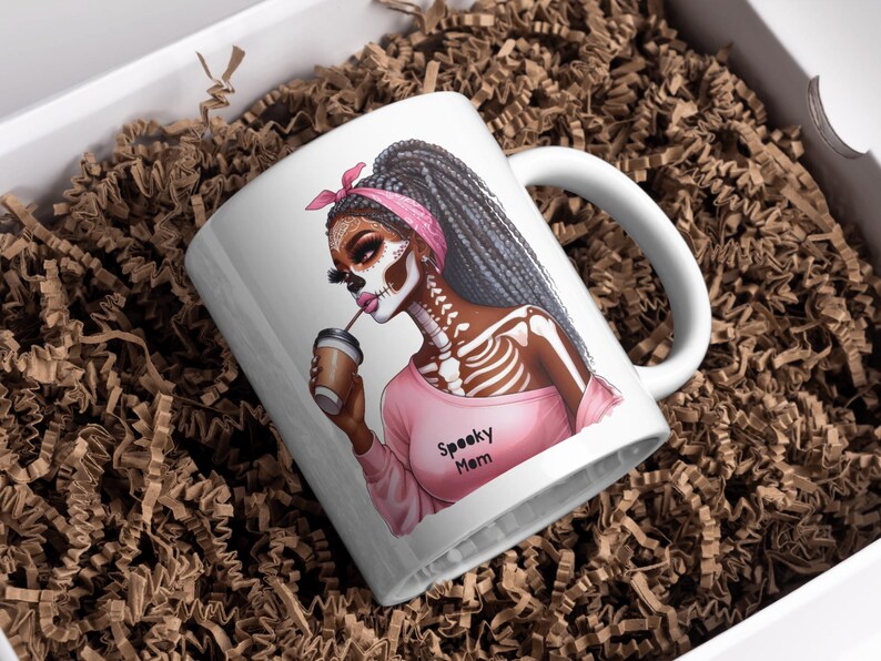 May include: White ceramic coffee mug with a pink and black illustration of a woman with a skeleton design and the text "Spooky Mom".