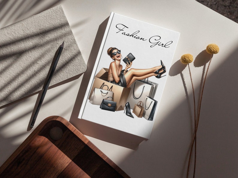 May include: A white notebook with the text "Fashion Girl" in black cursive script. The notebook features an illustration of a woman sitting in a box with shopping bags and wearing a black dress, sunglasses, and high heels.