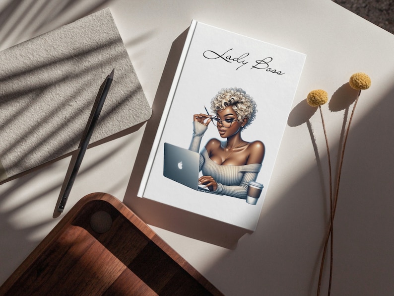 May include: A white notebook with the text "Lady Boss" in black cursive script. The notebook features an illustration of a woman with blonde hair wearing glasses and a white sweater, sitting at a desk with a laptop and a cup of coffee.