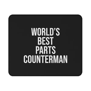 May include: A rectangular black mouse pad featuring the white text WORLD'S BEST PARTS COUNTERMAN centered in a clean, sans-serif font. The mouse pad has rounded corners and a stitched edge, providing a functional surface for computer mouse use.