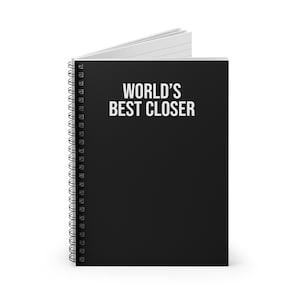 以下が含まれることがあります： 表紙に白い文字で「WORLD'S BEST CLOSER」とプリントされた黒いスパイラル綴じのノート。ノートは少し開いた状態で、左側の黒いワイヤー綴じの内側に白い罫線入りのページが見えています。