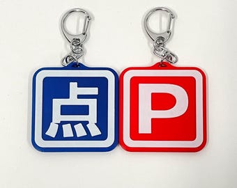 May include: Two keychains with blue and red square-shaped tags. The blue tag has a white Japanese character on it. The red tag has a white letter "P" on it.