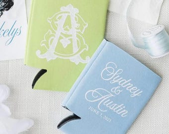 May include: Two beverage insulators, one light green with a white monogram and one light blue with the names "Sydney & Austin" and the date "June 7, 2025" in white script. The insulators are on a white surface.