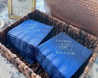May include: A wicker basket filled with stacks of navy blue napkins with the names "Lauren and William" printed in white script.