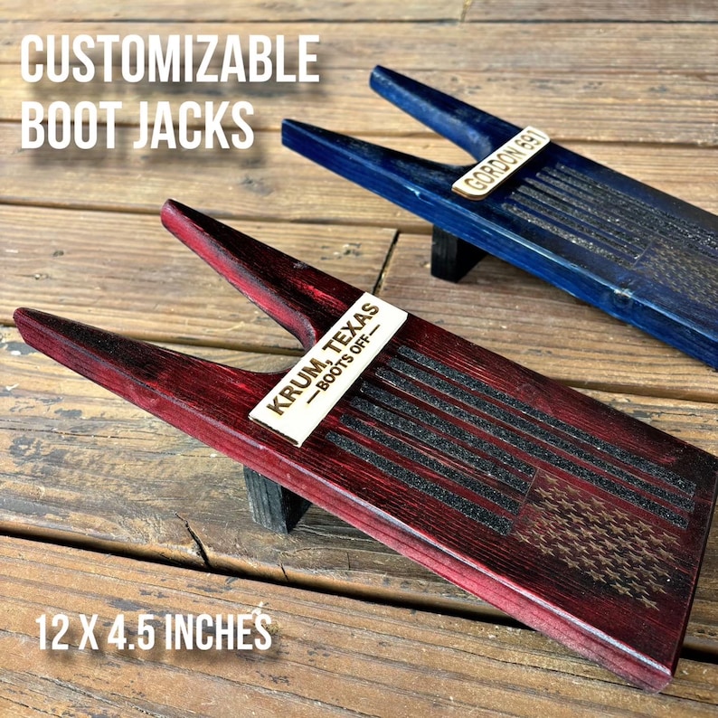 May include: Two wooden boot jacks with a distressed wood finish. The red boot jack has a wooden plaque with the text "KRUM, TEXAS - BOOTS OFF" and an American flag design. The blue boot jack has a wooden plaque with the text "GORDON BAY". Both boot jacks are 12 x 4.5 inches.