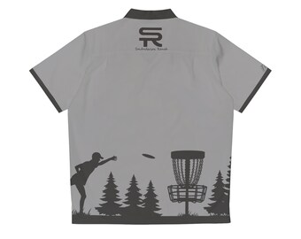Op de afbeelding: Grijs, kort, knoopsluiting overhemd met een zwarte kraag en afwerking. Het shirt heeft een silhouet van een persoon die een schijf gooit naar een discgolfmand met bomen op de achtergrond. De tekst "SR Sanderson Ranch" is gedrukt op de achterkant van het shirt.