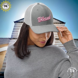 Puede incluir: Una gorra de camionero gris y blanca con un diseño bordado en rosa "Blessed". La gorra tiene una parte trasera de malla y una visera curvada.