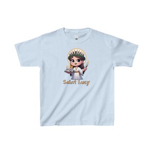 May include: Light blue t-shirt with a cartoon illustration of Saint Lucy, a young girl wearing a white dress and a crown of candles, holding a plate of candles and a lit candle. The text "Saint Lucy" is printed below the illustration.